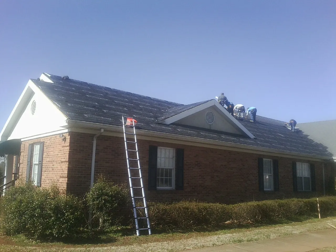 Crew tearing shingles off a brick ranch roof with a ladder set — Metal Roof Repair work by our crew in Bridgewater